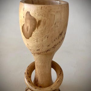 May include: A wooden goblet with a unique ring design on the base. The goblet is made of light brown wood with a natural grain pattern.