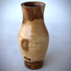 May include: A tall, turned wooden vase with a smooth, polished finish. The vase features a light tan body with darker brown wood grain patterns, a prominent knot, and three dark brown butterfly-shaped inlays securing a vertical crack.