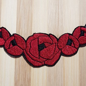 May include: A red embroidered flower patch with five flowers and two leaves. The flowers are arranged in a curved line and the leaves are on either end of the patch.