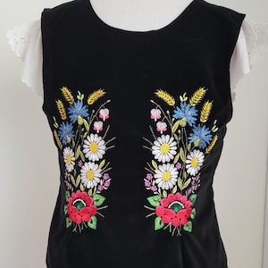 K&ouml;nnte beinhalten: Schwarze &auml;rmellose Weste mit gesticktem Blumendesign in Rot, Wei&szlig;, Gelb, Blau und Gr&uuml;n.