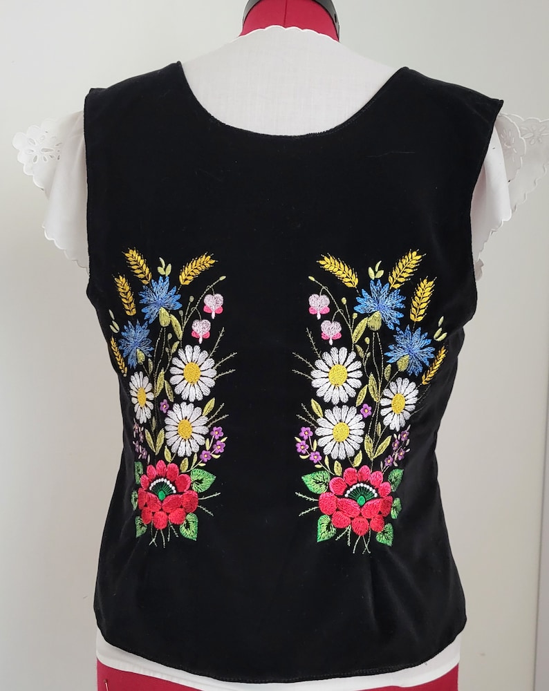 K&ouml;nnte beinhalten: Schwarze &auml;rmellose Weste mit gesticktem Blumendesign in Rot, Wei&szlig;, Gelb, Blau und Gr&uuml;n.