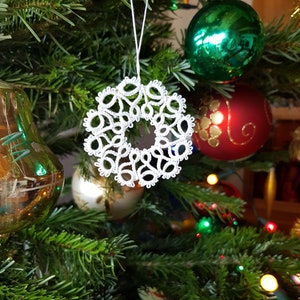 May include: A white crocheted snowflake ornament hanging on a Christmas tree with green needles and colorful ornaments.