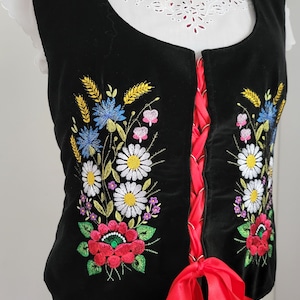K&ouml;nnte beinhalten: Eine schwarze Samt-Weste mit roter Schleife und gestickten Blumendesigns in Rot-, Wei&szlig;-, Blau-, Gelb- und Gr&uuml;nt&ouml;nen.