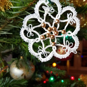 May include: White crocheted snowflake ornament with gold beads hanging on a green Christmas tree.