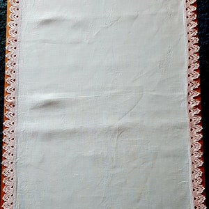 May include: A white linen tablecloth with a delicate pink crocheted border. The tablecloth is smooth and has a subtle sheen.