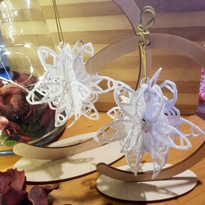 May include: Two white lace snowflake ornaments hanging from wooden stands. The snowflakes are delicate and intricate, with a lacy design.