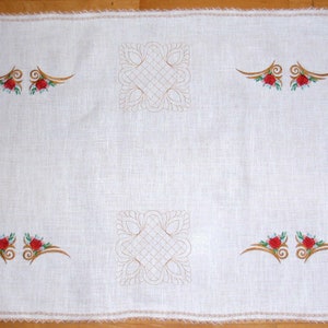 May include: White linen table runner with embroidered floral designs and a delicate lace trim. The design features a repeating pattern of stylized flowers and leaves in gold thread.