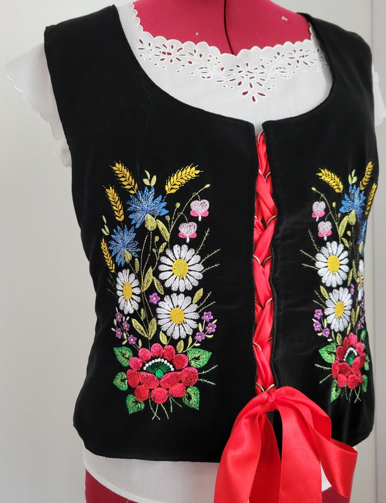 K&ouml;nnte beinhalten: Schwarze Samt-Weste mit roter Schleifen-Schn&uuml;rung und gesticktem Blumendesign mit roten, wei&szlig;en, blauen, gelben und gr&uuml;nen Blumen.