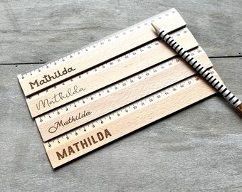 May include: Four wooden rulers stacked on top of each other. Each ruler has the name "Mathilda" engraved on it in a different font style. The rulers are marked with numbers from 0 to 20.