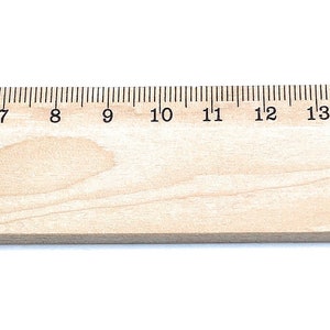 May include: A wooden ruler with a personalised inscription that reads "Emilia". The ruler is 20 centimetres long and has markings for each centimetre.