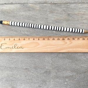 May include: A wooden ruler with black and white markings and the name "Emilia" engraved on it. The ruler is 20 centimetres long.