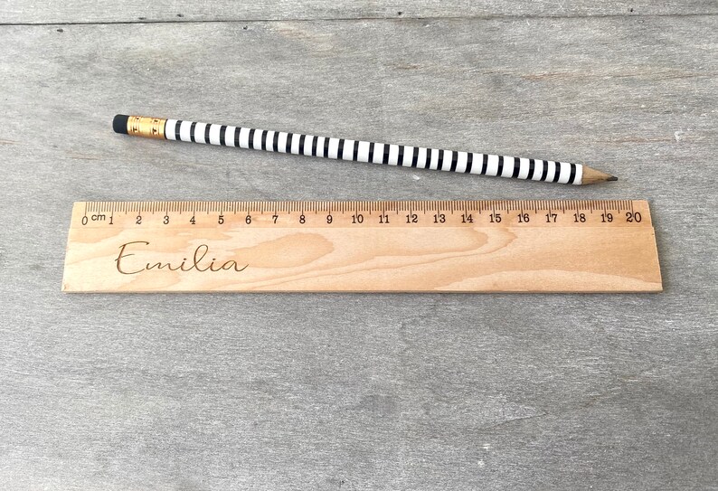 May include: A wooden ruler with black and white markings and the name "Emilia" engraved on it. The ruler is 20 centimetres long.
