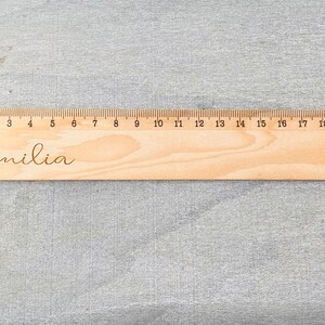 May include: A wooden ruler with a 20 cm scale and the name "Emilia" engraved on it.