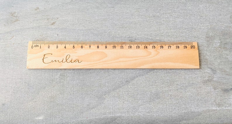 May include: A wooden ruler with a 20 cm scale and the name "Emilia" engraved on it.