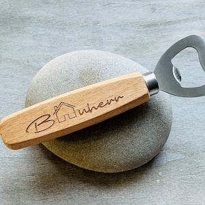 Könnte beinhalten: Ein Flaschenöffner aus Holz mit einem Metallöffner und einem Holzgriff. Der Griff ist mit dem Text "Home Where" und einem kleinen Haussymbol graviert.