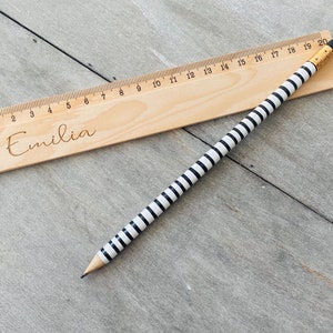 May include: A wooden ruler with black and white stripes and the name "Emilia" engraved on it. The ruler is 20 centimetres long and has markings for each centimetre.