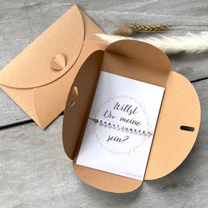 Bracelet et carte de demande de demoiselle d'honneur dans une enveloppe kraft avec fermeture en forme de cœur