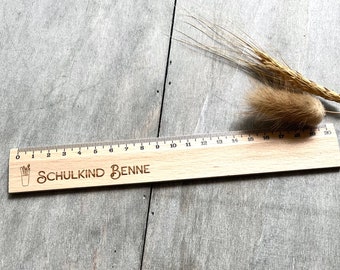Könnte beinhalten: Ein Holzlineal mit einem schwarz-weißen Design von Bleistiften in einer Tasse und dem Text "SCHULKIND BENNE" auf der Vorderseite. Das Lineal ist 50,8 cm lang und hat Markierungen für jeden Zentimeter.