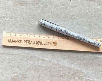 May include: A wooden ruler with a heart and the text "DANKE, FRAU MÜLLER" engraved on it. A white pen with black polka dots is lying on top of the ruler.