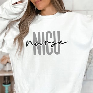 Puede incluir: Sudadera blanca con el texto "NICU nurse" en letras negras y grises.