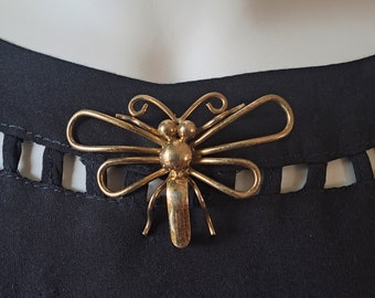 May include: A gold-toned metal dragonfly brooch with intricate details. The wings are curled and the body is textured.