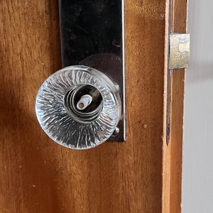 May include: A close-up of a vintage glass doorknob with a textured surface. The doorknob is attached to a wooden door with a silver door handle.