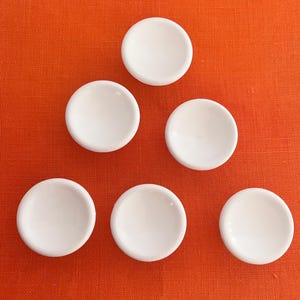 May include: Six white ceramic bowls arranged in a triangular pattern on an orange background.