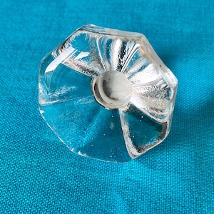 Op de afbeelding: Een glazen flesstopper van helder glas met een facetgeslepen ontwerp. De stopper heeft een ronde opening in het midden.