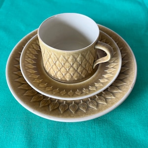 May include: A set of three ceramic plates with a green and brown leaf pattern. The plates are nested together, with the smallest plate on top. The plates are made of a textured ceramic and have a slightly raised edge.