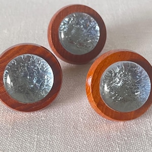 May include: Three round wooden cabinet knobs with a clear, textured glass center. The wood is a warm brown color, and the glass has a frosted appearance. These knobs are likely for furniture or decorative use.