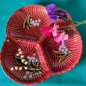 May include: A three-sectioned serving dish with a burgundy glaze and floral designs. The dish features a raised, textured design and is decorated with white and blue flowers.