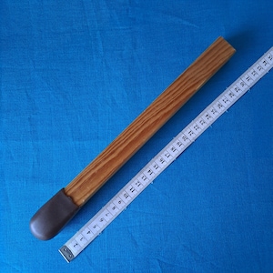 May include: A wooden stick with a brown leather tip, measured with a white tape measure. The stick is approximately 35 inches long.