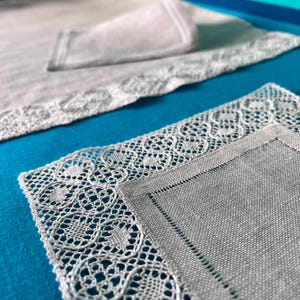 Może przedstawiać: Dwa białe obrusy lniane z delikatną koronką. Obrusy leżą na jasnoniebieskiej powierzchni.