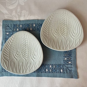 May include: Two white ceramic plates with a geometric design. The plates have a raised pattern of lines and curves, creating a textured surface.