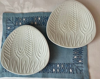 May include: Two white ceramic plates with a geometric design. The plates have a raised pattern of lines and curves, creating a textured surface.