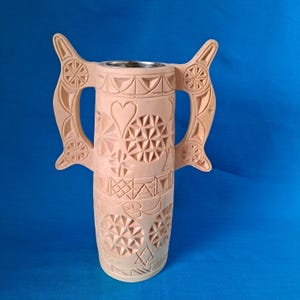 May include: A hand-carved wooden vase with two handles and intricate geometric patterns. The vase is a light brown color and has a smooth, polished finish.