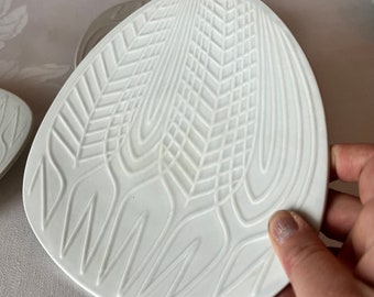 May include: White ceramic plate with a raised design of stylized wheat stalks. The plate is oval shaped and has a smooth, glossy finish.