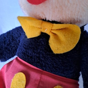 Puede incluir: Un juguete de peluche de Mickey Mouse con un cuerpo de piel negra, pantalones cortos rojos con botones amarillos y una pajarita amarilla.