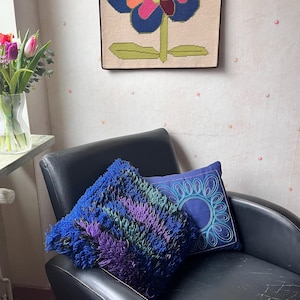 May include: A black leather armchair with two throw pillows. One pillow is blue with a white circular design, and the other is a fluffy, blue, purple, and green pillow.