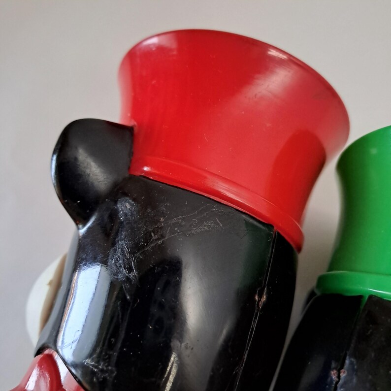 May include: Close-up of two vintage toy figures. One figure has a red hat and black body, the other has a green hat and black body. The figures are made of plastic and have a glossy finish.
