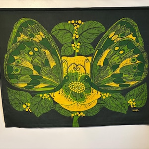 Puede incluir: Un tapiz de pared verde oscuro con un diseño simétrico que presenta dos grandes mariposas con alas verdes y amarillas. Las mariposas están colocadas alrededor de una flor amarilla con hojas verdes y pequeñas bayas amarillas. La palabra "ULLAS" está en la esquina inferior derecha.