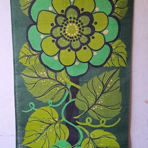 Puede incluir: Un tapiz floral verde con una barra de metal en la parte superior. El diseño presenta una gran flor en tonos verdes y chartreuse, con detalles en negro y hojas estilizadas. El fondo es de color verde oscuro.