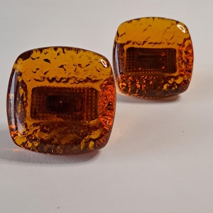 May include: Two square amber glass cabinet knobs. Each knob has a textured surface and a rectangular design in the centre. The knobs are a warm, translucent orange colour.