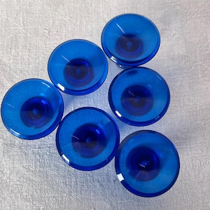 Könnte beinhalten: Sechs kreisförmige Objekte aus kobaltblauem Glas mit einer zentralen Vertiefung und ausgestellten Rändern. Die Objekte sind transparent und auf einer hellen Oberfläche angeordnet. Jedes Objekt hat einen tiefen, lebendigen Blauton.