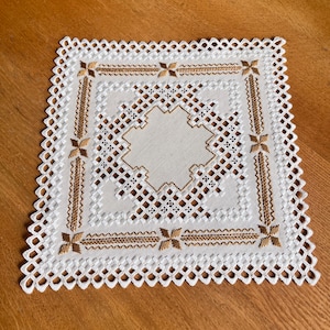Peut inclure: Nappe carrée brodée blanche et dorée avec bordure festonnée. Le centre présente un motif géométrique avec des accents dorés. Les coins ont des motifs floraux dorés et les bords sont finement détaillés.