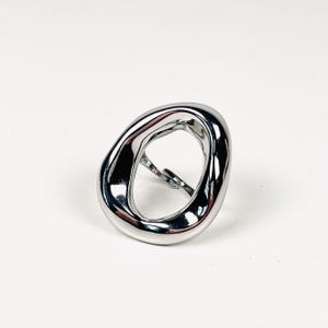 May include: A shiny, silver-colored ring with an abstract, open design. The ring has a smooth, polished surface and a unique, irregular shape. The ring is a piece of jewelry.