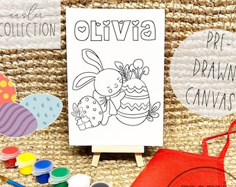 May include: A pre-drawn canvas with the name "Olivia" above a black and white Easter bunny design. The image includes paint pots, a paintbrush, and a red apron. The words "Easter Collection" are in the upper left corner.