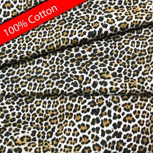 Pu&ograve; includere: Un primo piano di un tessuto bianco con un motivo a stampa leopardata marrone e nero. Il tessuto &egrave; etichettato come 100% cotone.