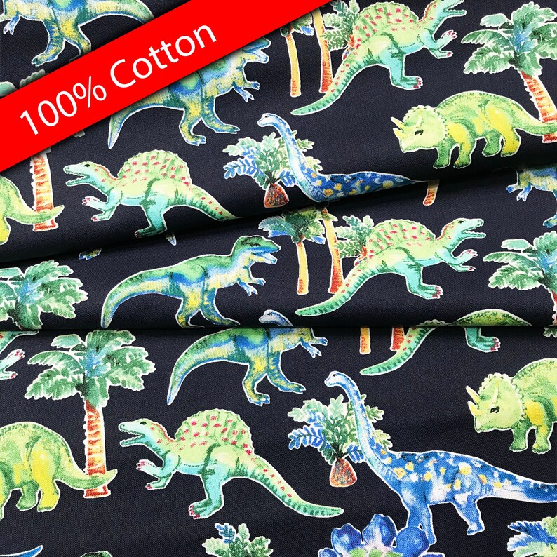 Pu&ograve; includere: Un tessuto blu navy con un motivo ripetuto di dinosauri verdi e blu e palme. Il tessuto ha la scritta "100% Cotone" stampata su di esso.