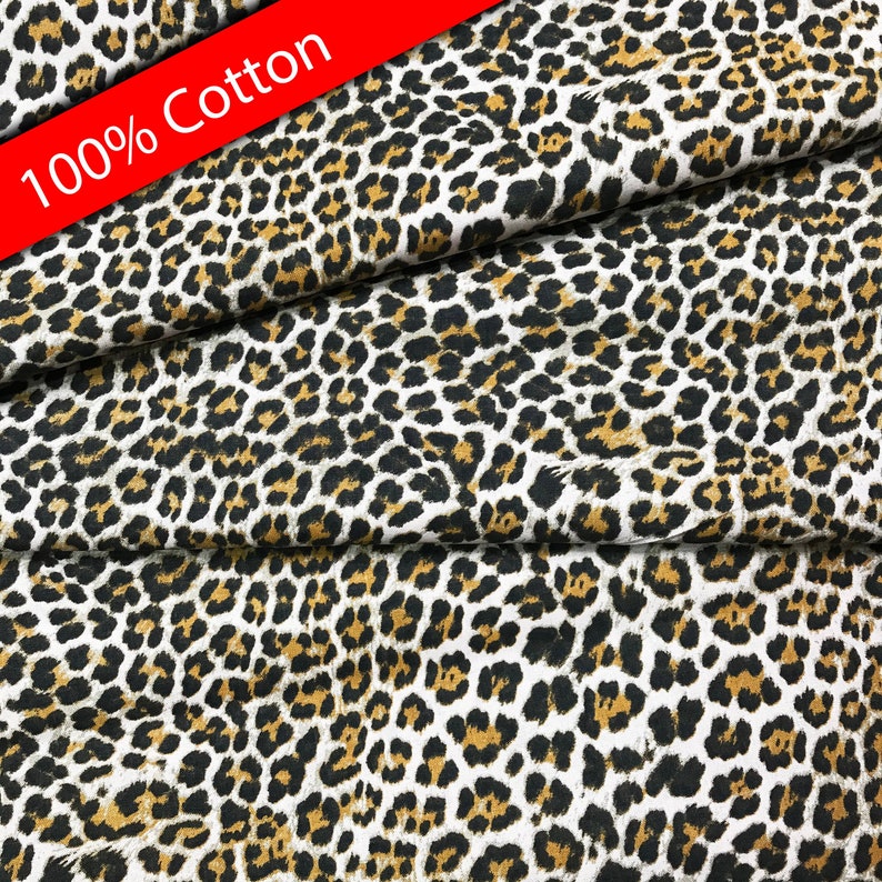 Pu&ograve; includere: Un primo piano di un tessuto bianco con un motivo a stampa leopardata marrone e nero. Il tessuto &egrave; etichettato come 100% cotone.